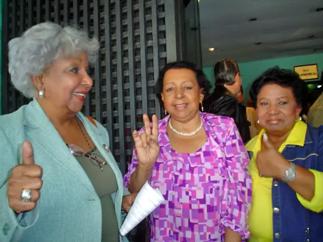 Tres mujeres celebran y saludan a la cámara durante un evento