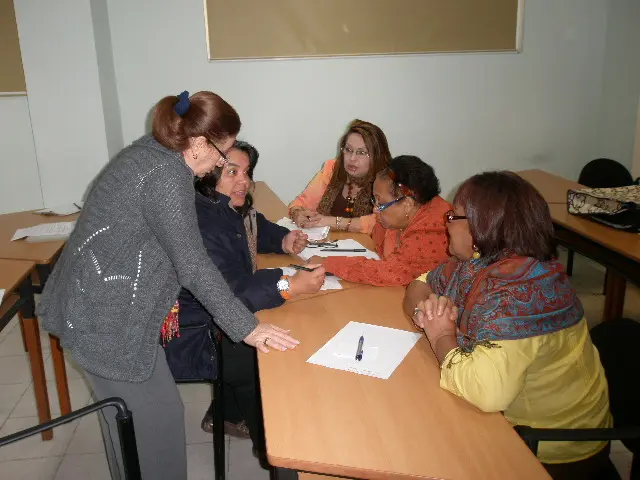 Una facilitadora acompaña a un grupo de participantes reunidas alrededor de una mesa de trabajo